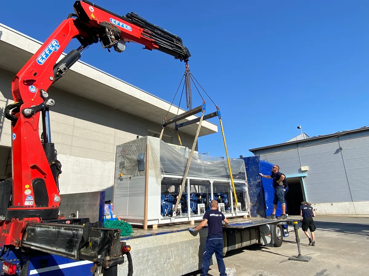 Ein Kran hebt eine Wärmepumpe von der Ladefläche eines Sattelschleppers.